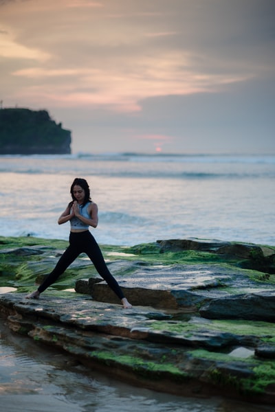 在水旁边的岩石平台上做瑜伽的女人